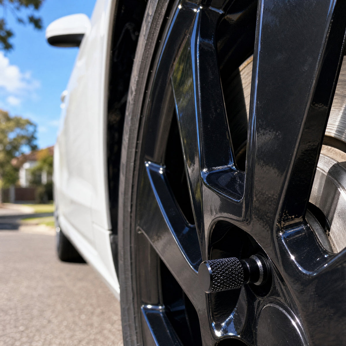 Black aluminium valve cap on a gloss black alloy wheel of a white hatchback