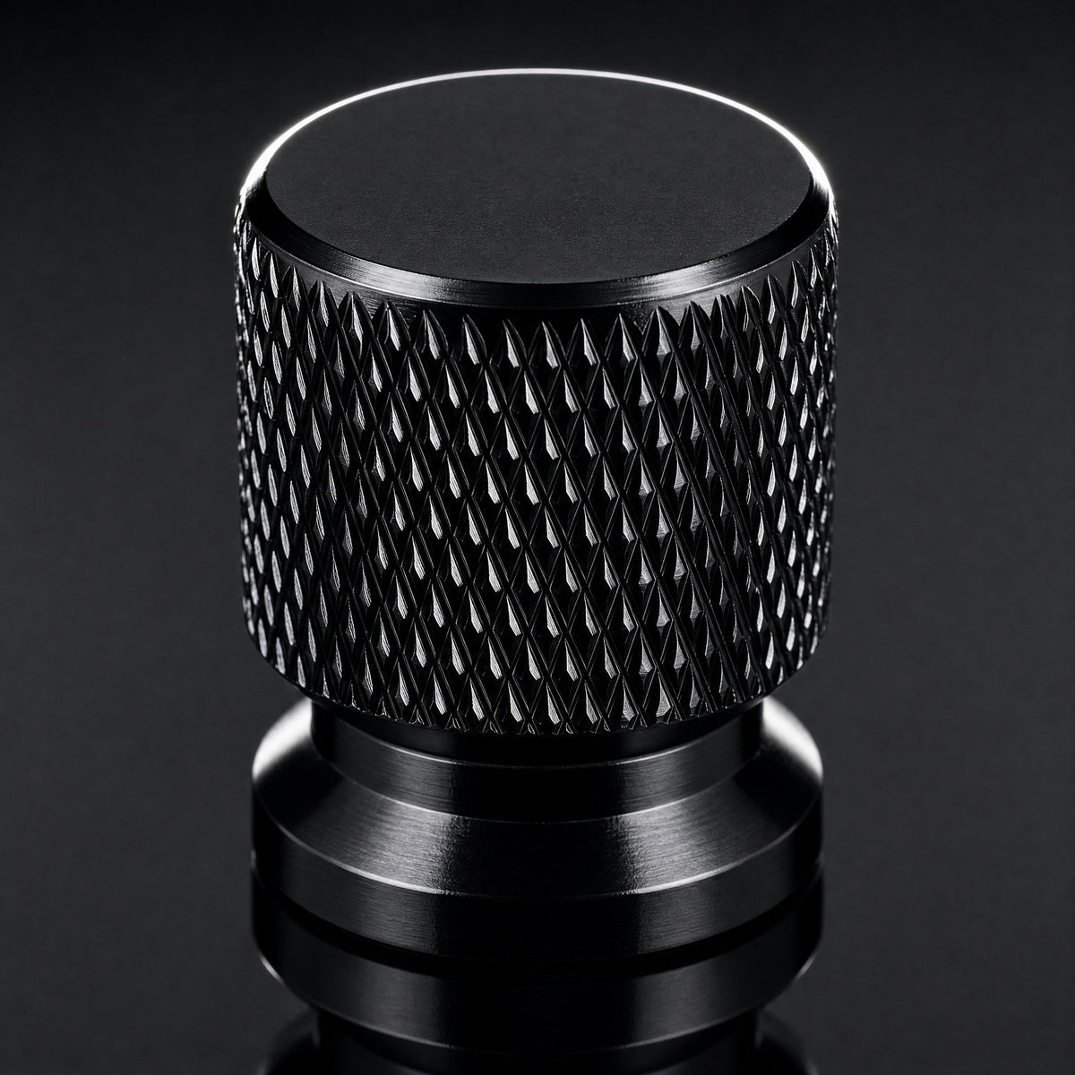 Close-up of a black anodised aluminium valve cap showing the machined diamond knurl and chamfered top
