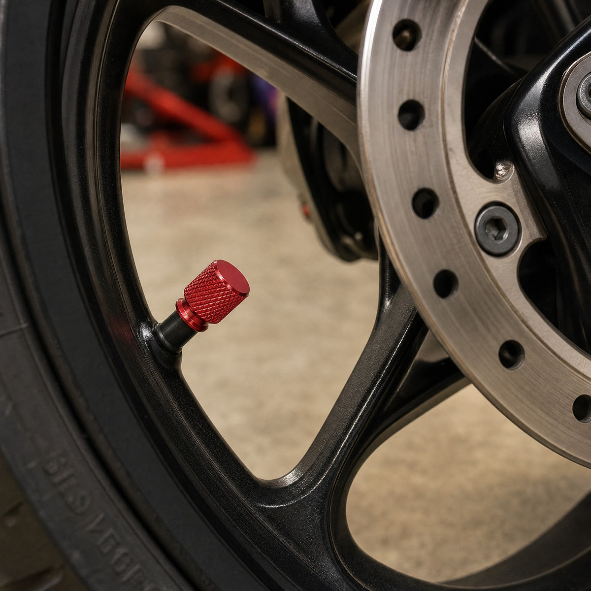 Red aluminium valve cap on a motorcycle wheel valve beside the brake disc